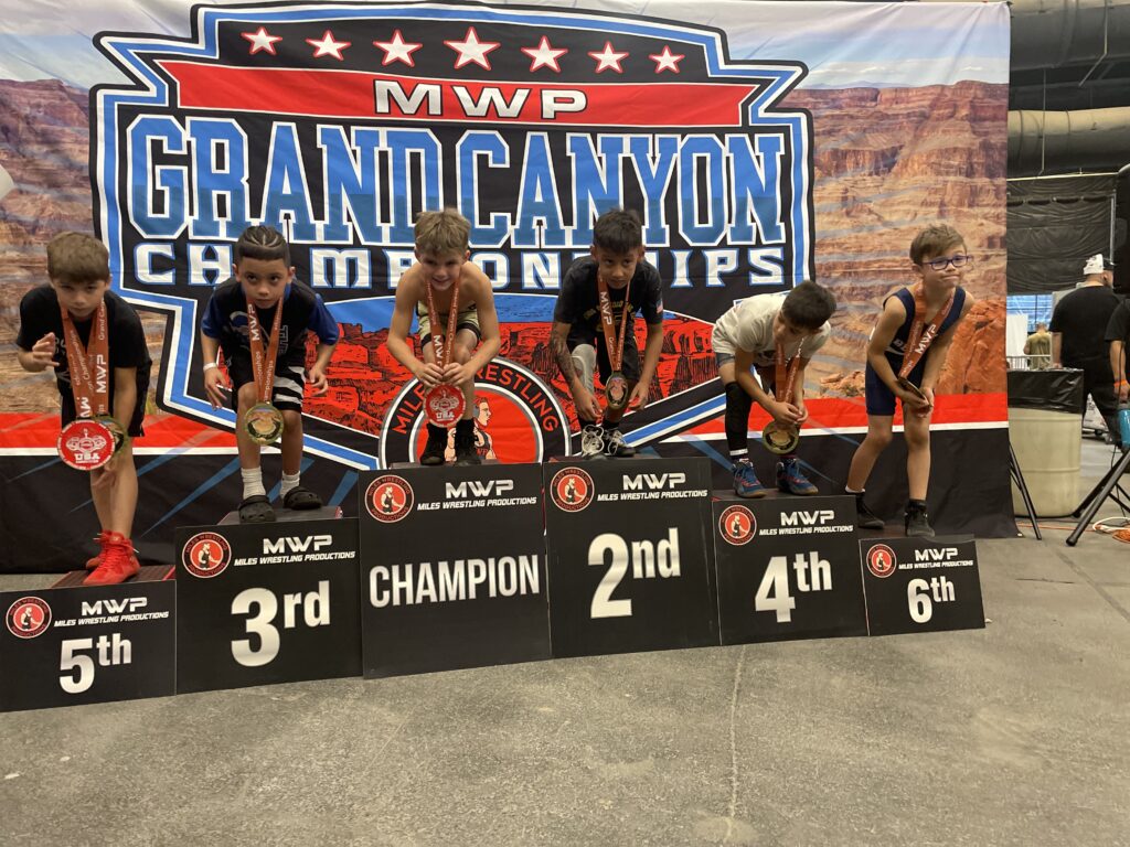 Youth sports wrestlers celebrating and flexing their muscles at the winners podium.